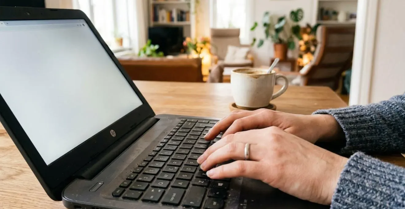 Detalle de manos tecleando en un portátil junto a una taza de café, en un ambiente doméstico luminoso